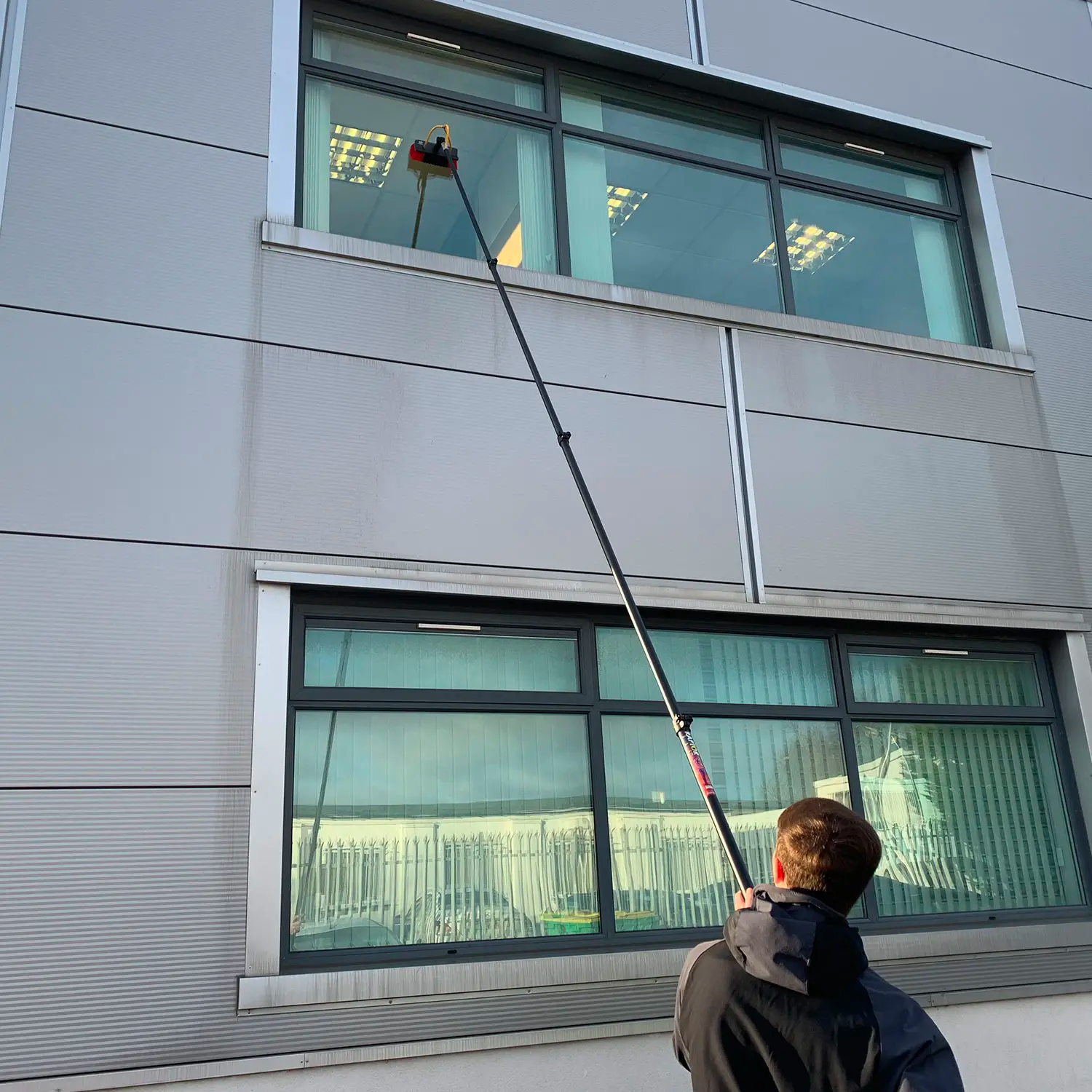 Commercial window cleaner using a water-fed extension pole to clean second-story office windows — practical application of commercial window cleaning tips.