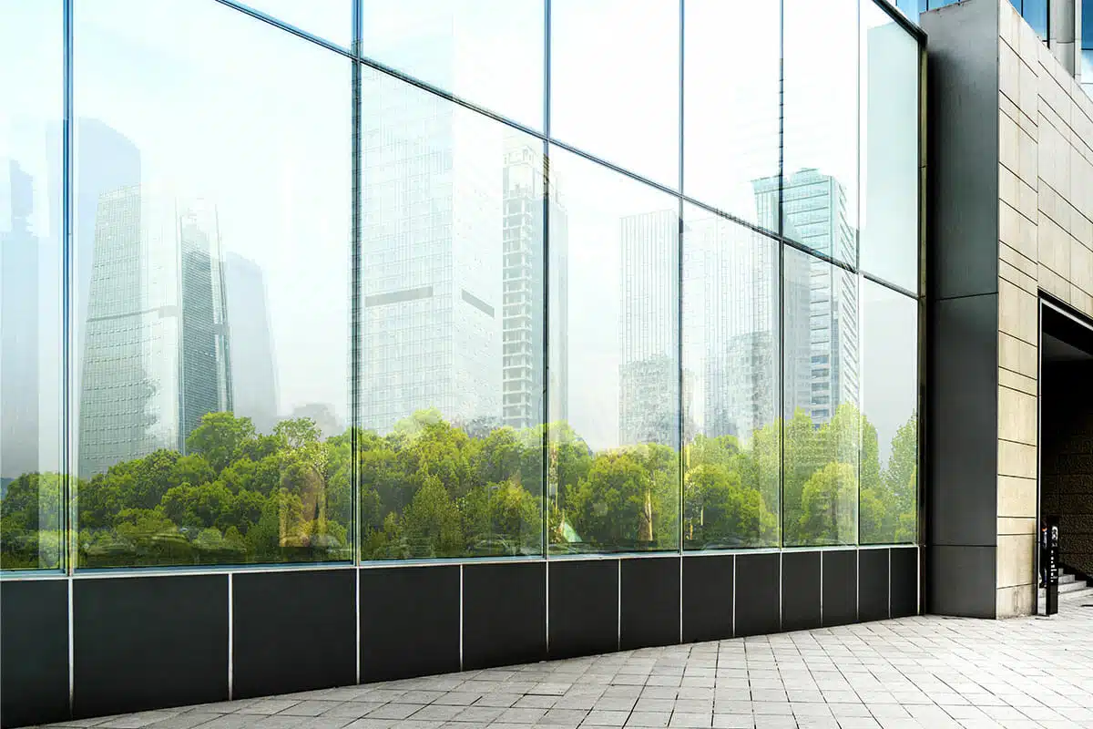 Spotless commercial glass building reflecting trees and skyscrapers — ideal result of expert commercial window cleaning tips.